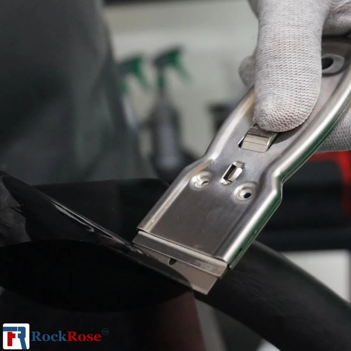 Person wearing gloves using a Steel Razor Scraper on a vehicle component with RockRose logo.