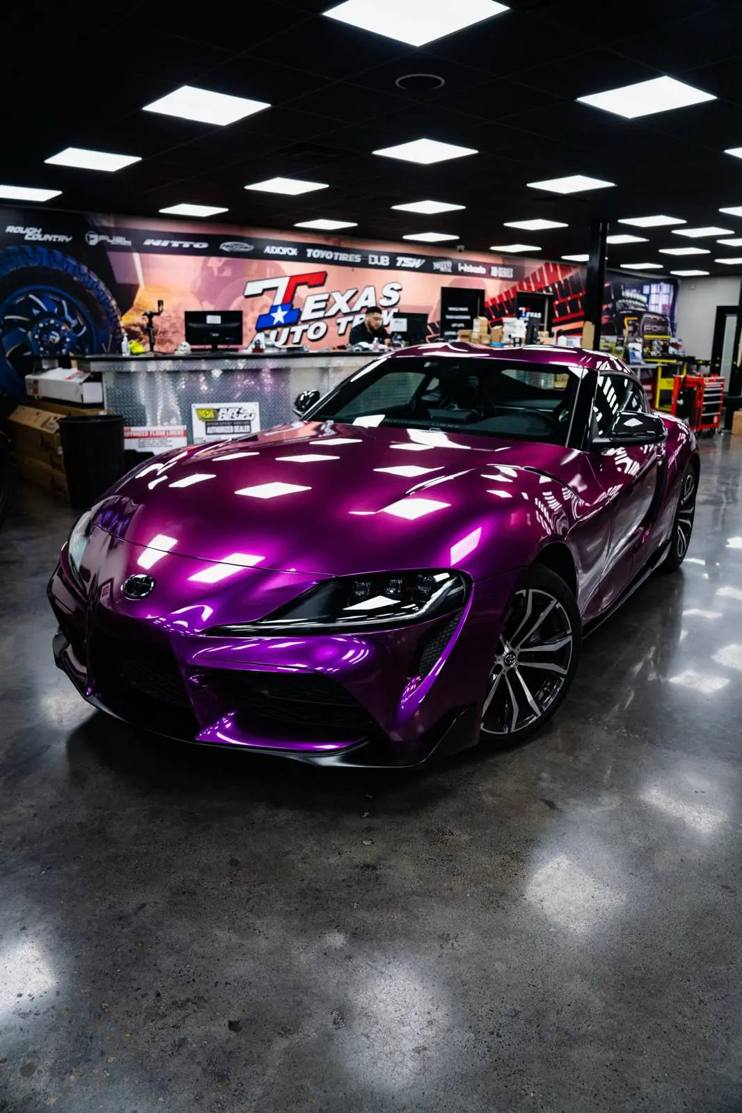 Purple sports car in a showroom with 'Texas Auto Body' in the background color pansy