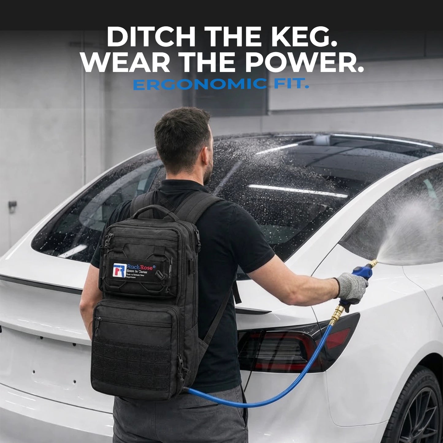 A man wearing a black ergonomic backpack with a blue hose connected to it, washing a white car in a garage. 