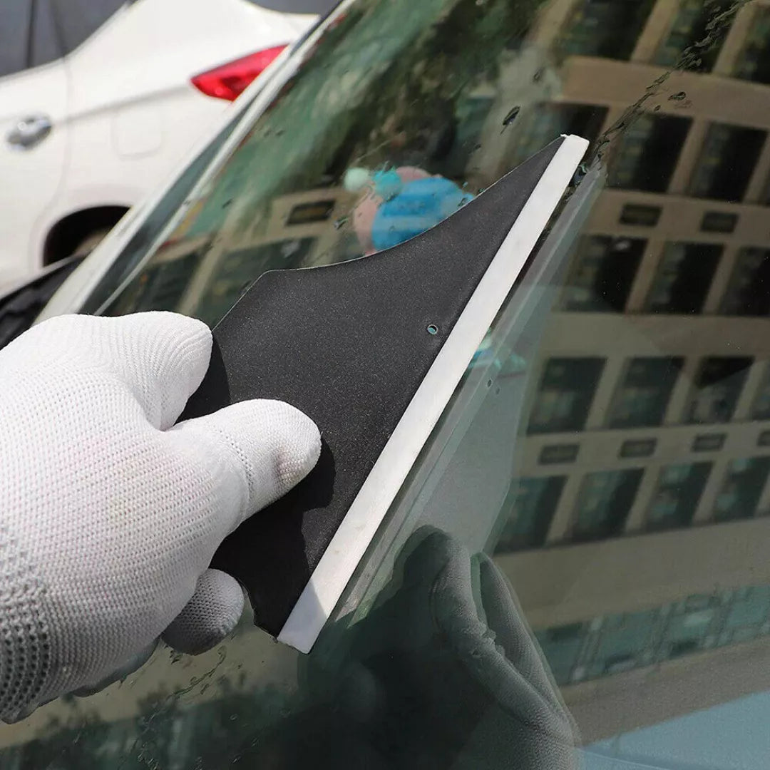 Person using a squeegee on a car window with a blurred cityscape in the background