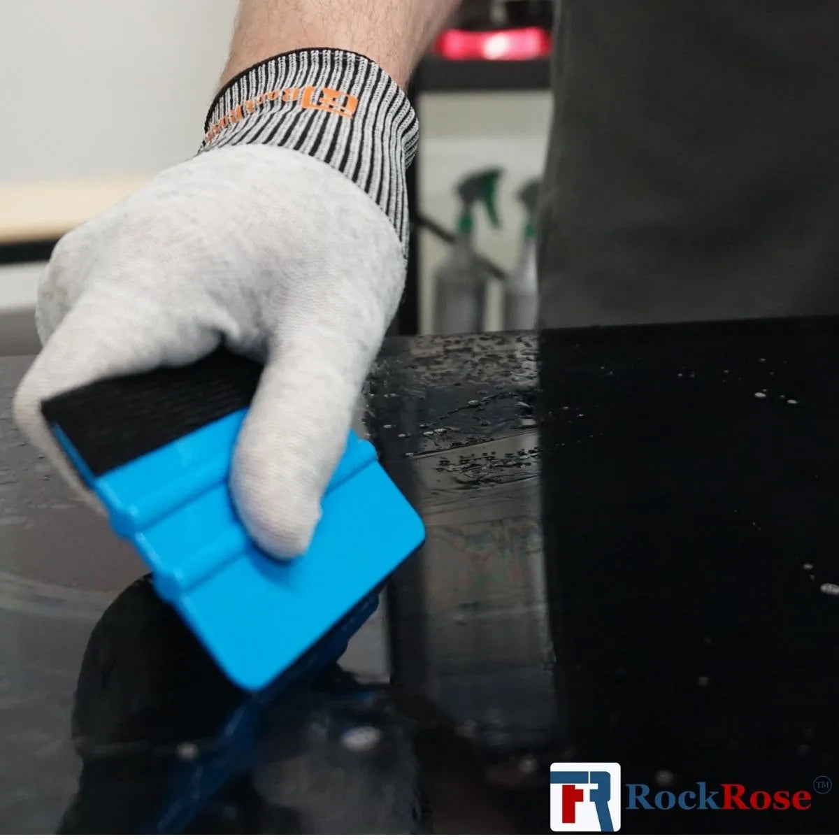 Hand wearing a white glove holding a blue squeegee over a car window with RockRose logo.