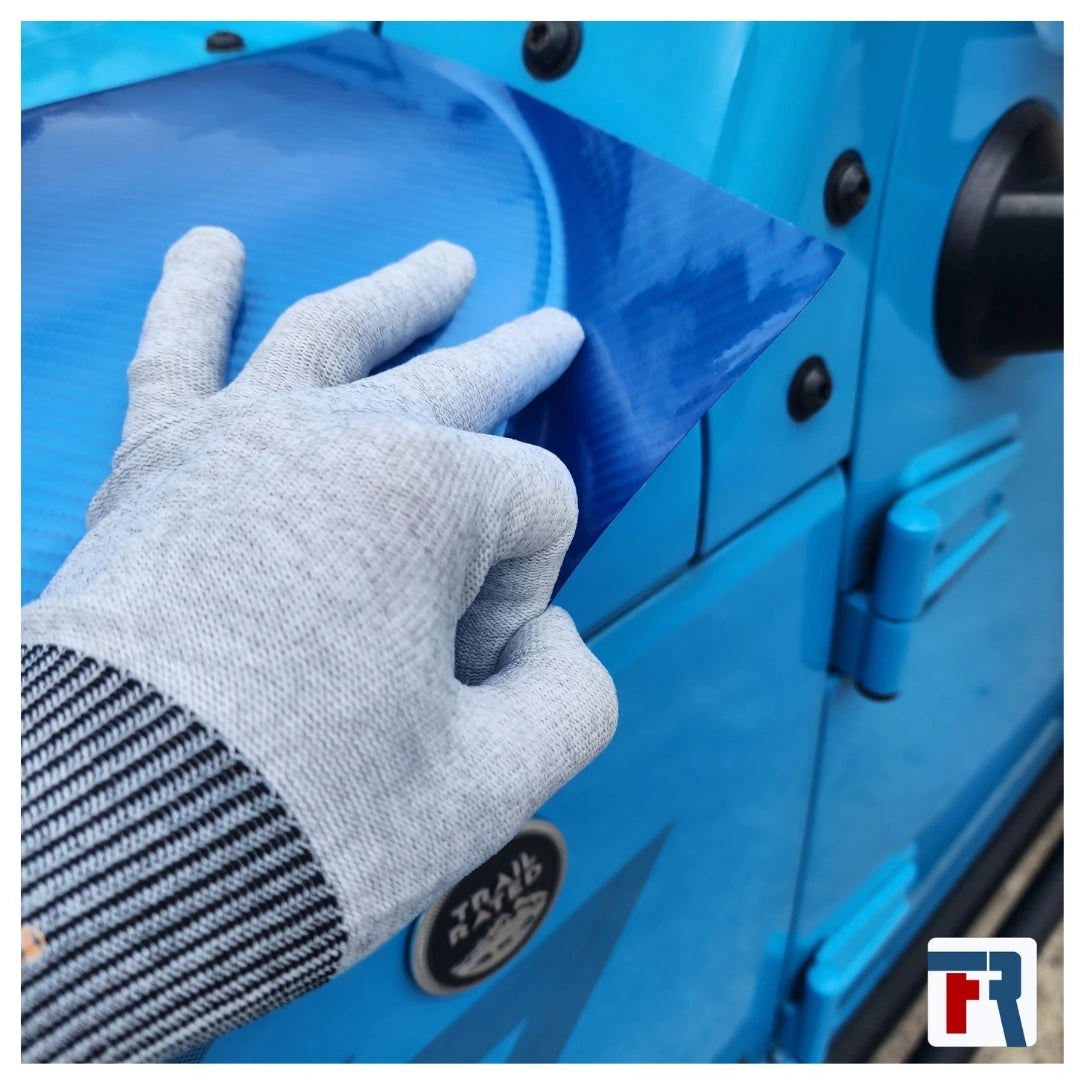 Person applying a blue protective film to a blue vehicle door with a gray glove.
