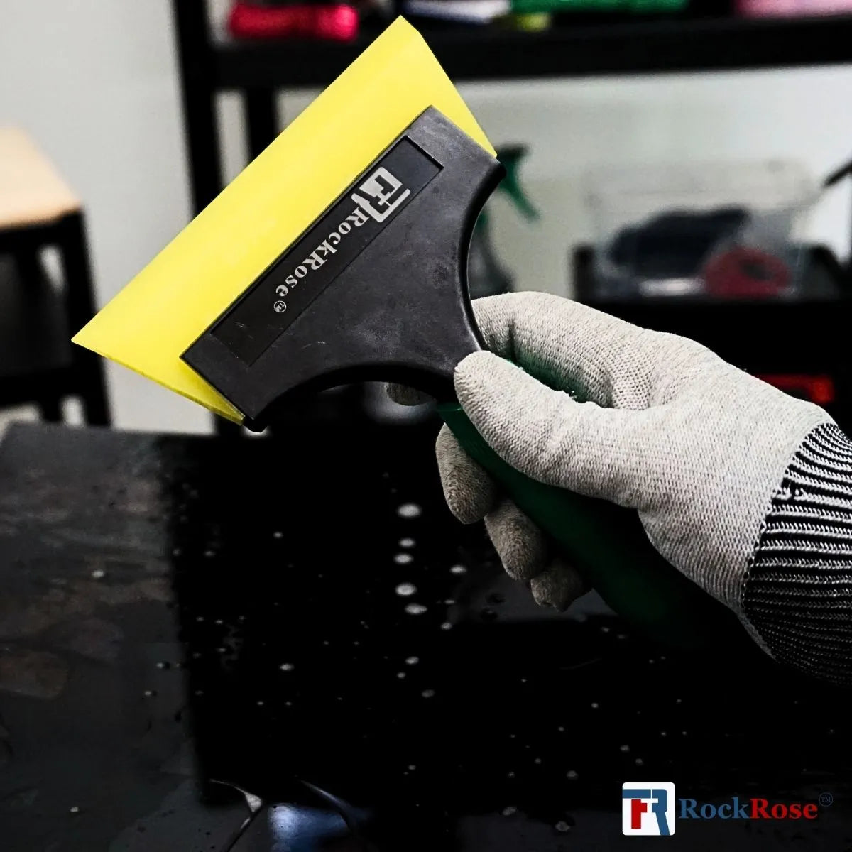 Holding a green squeegee using a glove with yellow tint scrapper and rockrose logo 