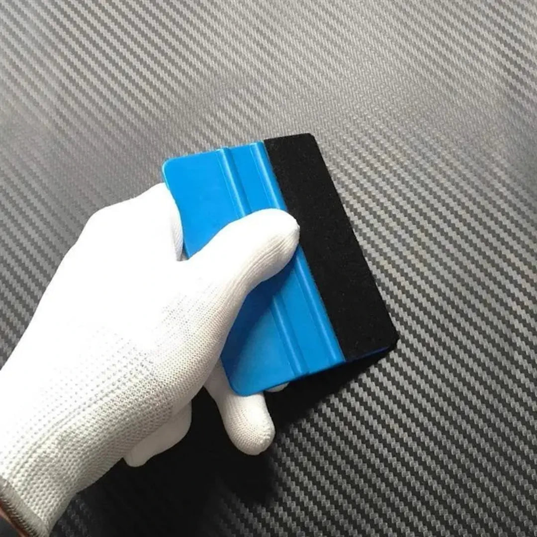 White gloves using blue squeegee on a carbon fiber vinyl wrap