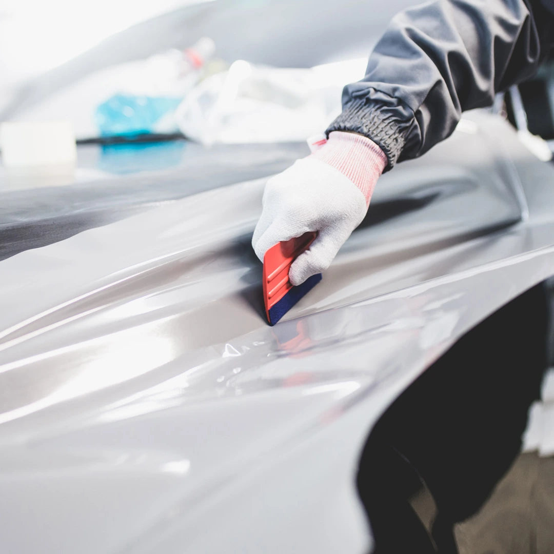 Person applying car wrap to a vehicle with a red squeegee tool
