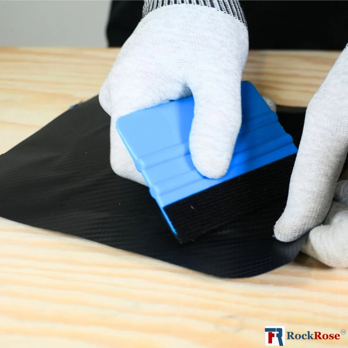 Person using a blue sanding squeegee block on black material with RockRose logo in the corner.