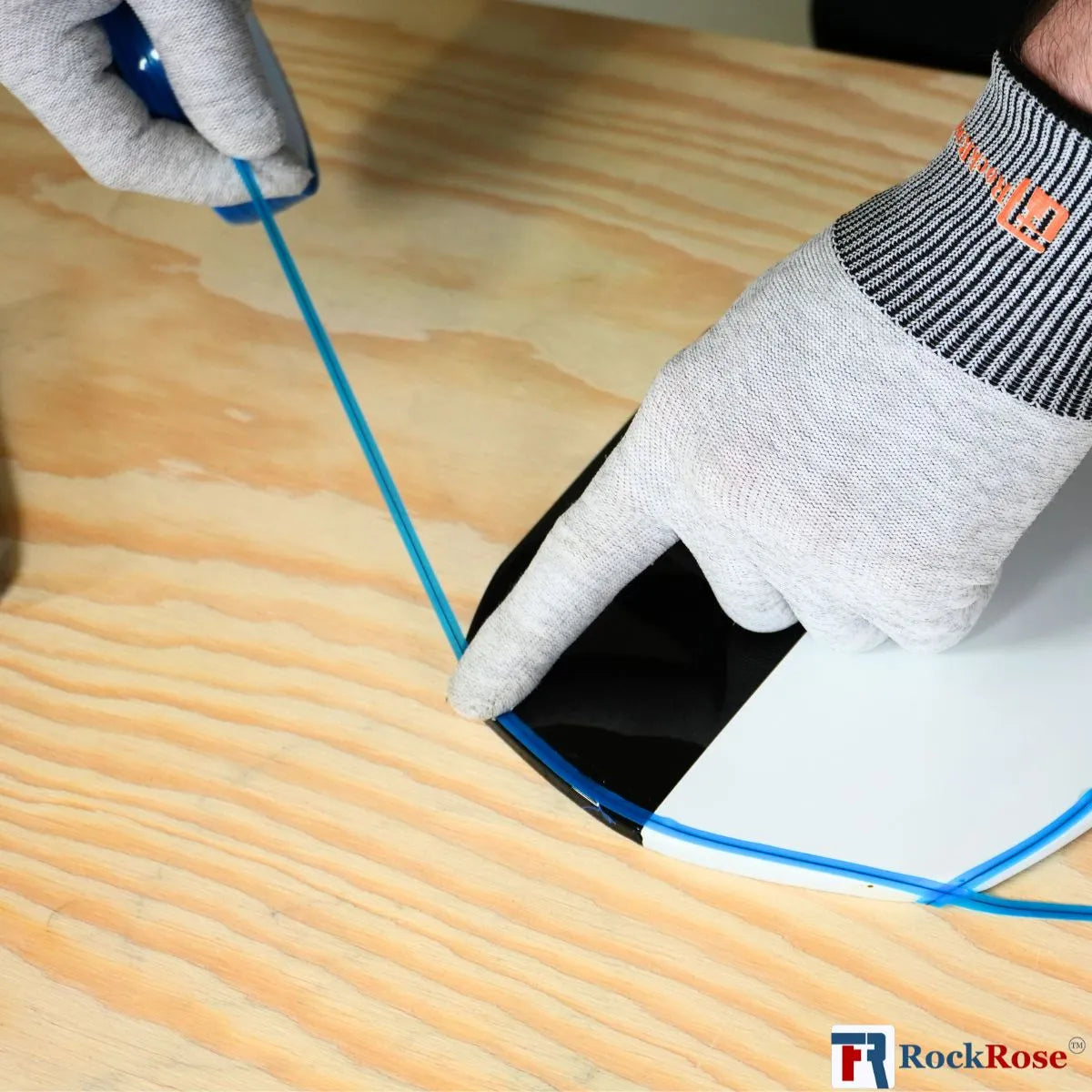 Person wearing gloves and using a tool on a wooden surface with RockRose logo.