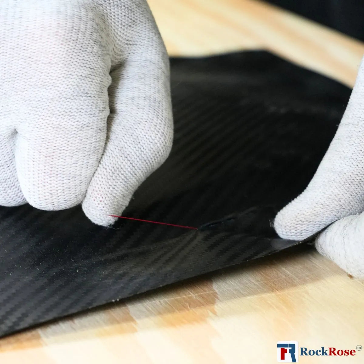 Person wearing gloves working on a carbon fiber surface with RockRose logo.