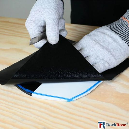 Person wearing gloves applying black material to a surface with a tool, on a wooden table.