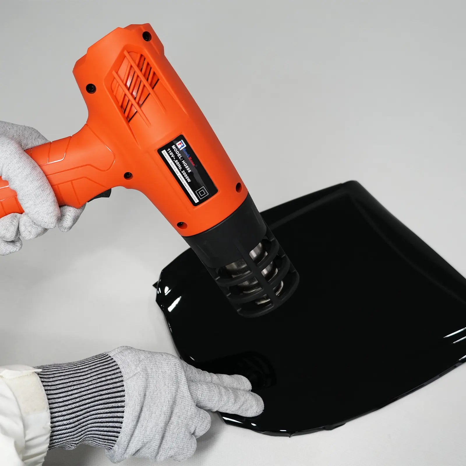 Person using an orange heat gun on a black object with a gray background