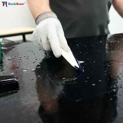 Person using a blue silicone tint squeegeee  to a black surface with a white glove.