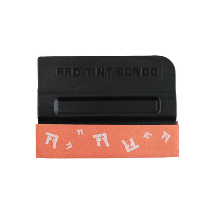 A black Wing Squeegee plastic Pro-Tint Bondo applicator tool resting on an orange sanding belt with white lettering, isolated on a white background.