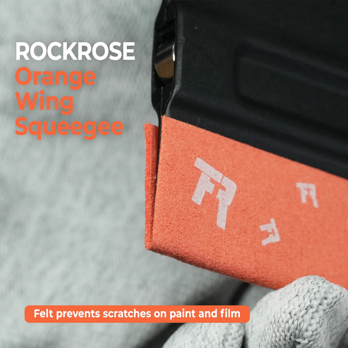 Close-up of an Rockrose Black felt wing squeegee being used on a black surface, with text reading 'ROCKROSE Black Wing Squeegee' and a note that felt prevents scratches on paint and film.