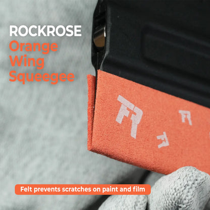 Close-up of an Rockrose Black felt wing squeegee being used on a black surface, with text reading 'ROCKROSE Black Wing Squeegee' and a note that felt prevents scratches on paint and film.