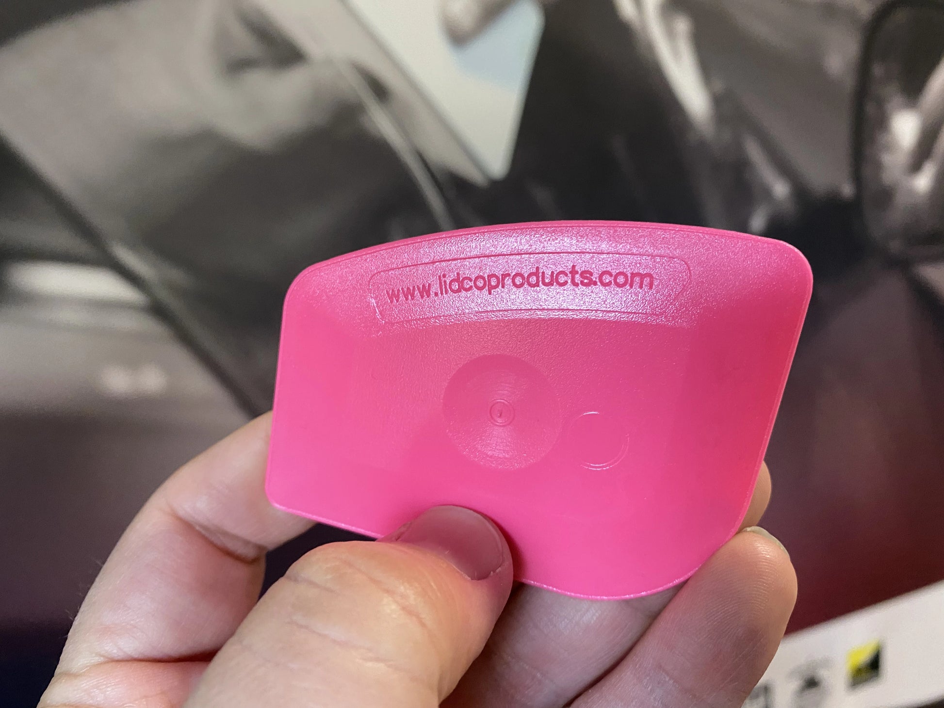 Pink car detailing tool held by a hand with a blurred background