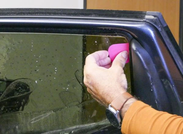 Person cleaning a car window with a pink sponge