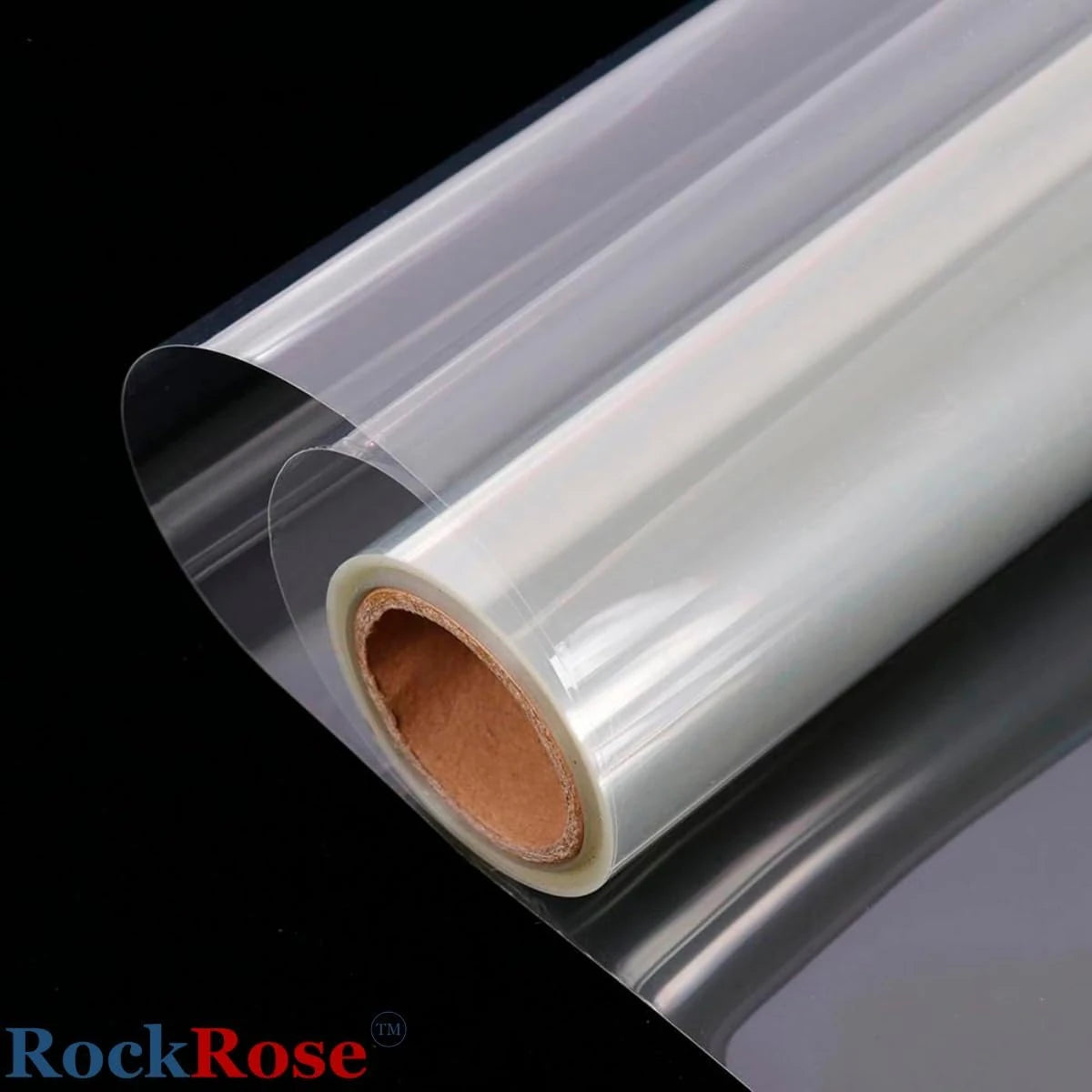 A roll of transparent plastic security window film partially unrolled, showing its clear material and brown cardboard core, photographed against a black background with a RockRose logo in the corner.