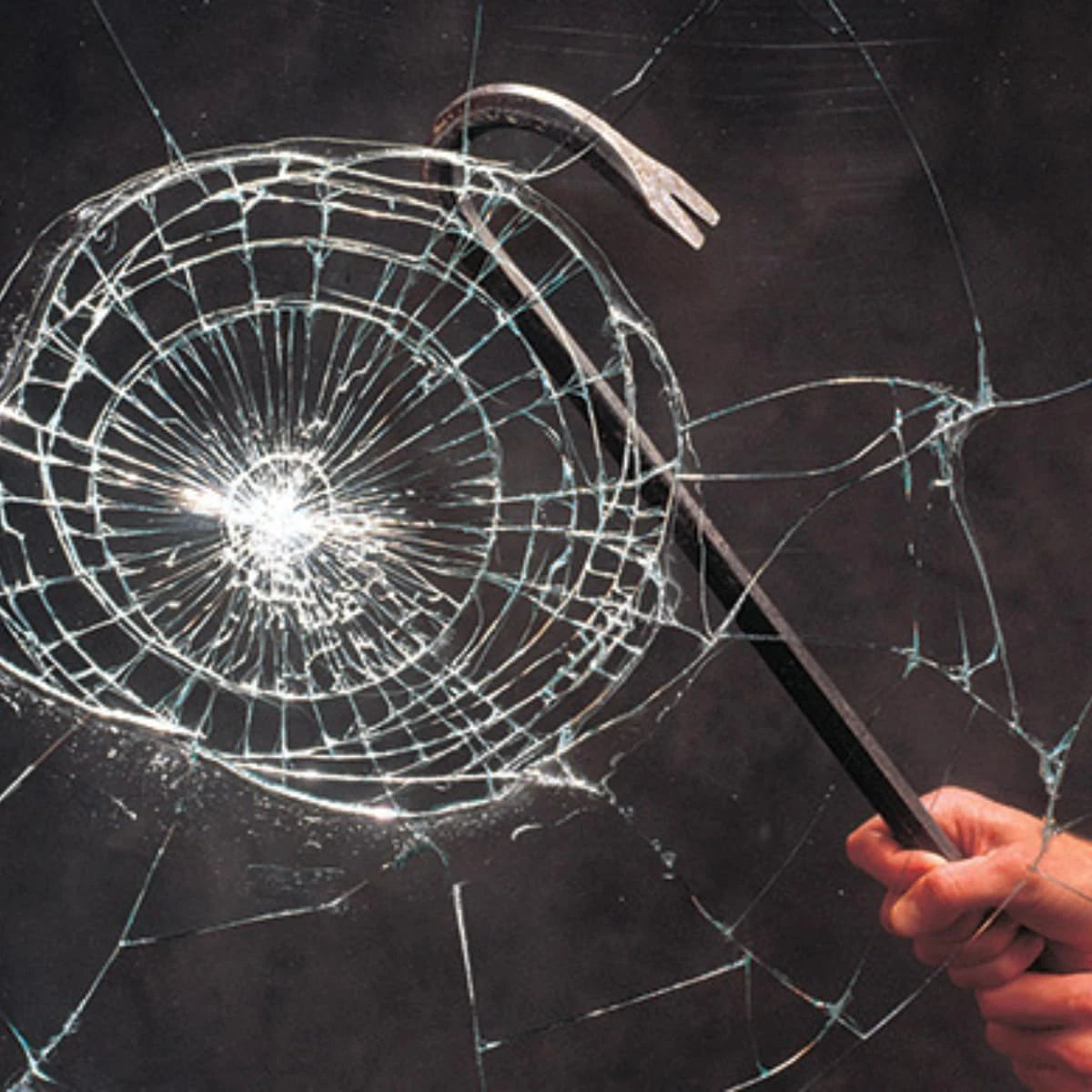 Hand holding a crowbar against a shattered glass window