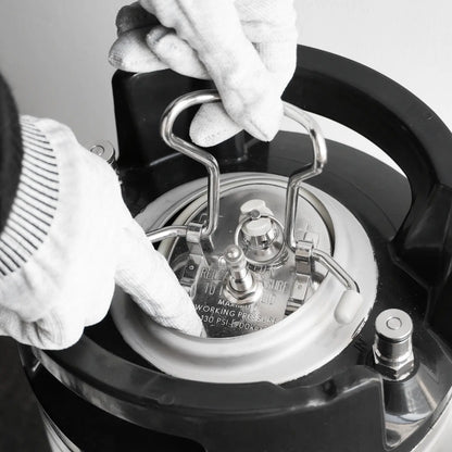 Close-up of gloved hands lifting the metal pressure release valve on a black appliance, likely a pressure cooker, in a monochrome photo.