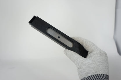 Black rectangular object held by a gloved hand on a light gray background