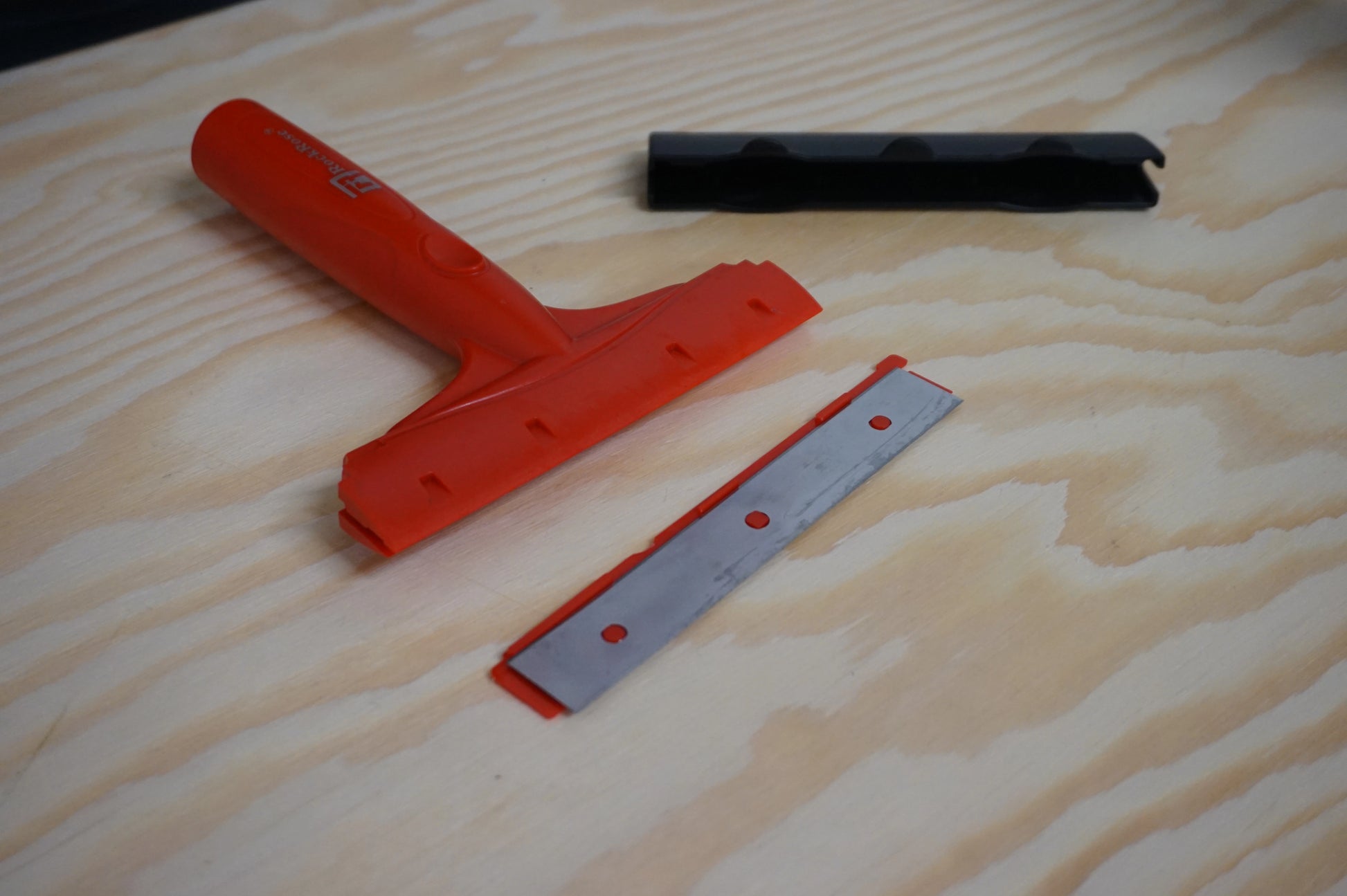 Red and black squeegee with blades tool on a wooden surface