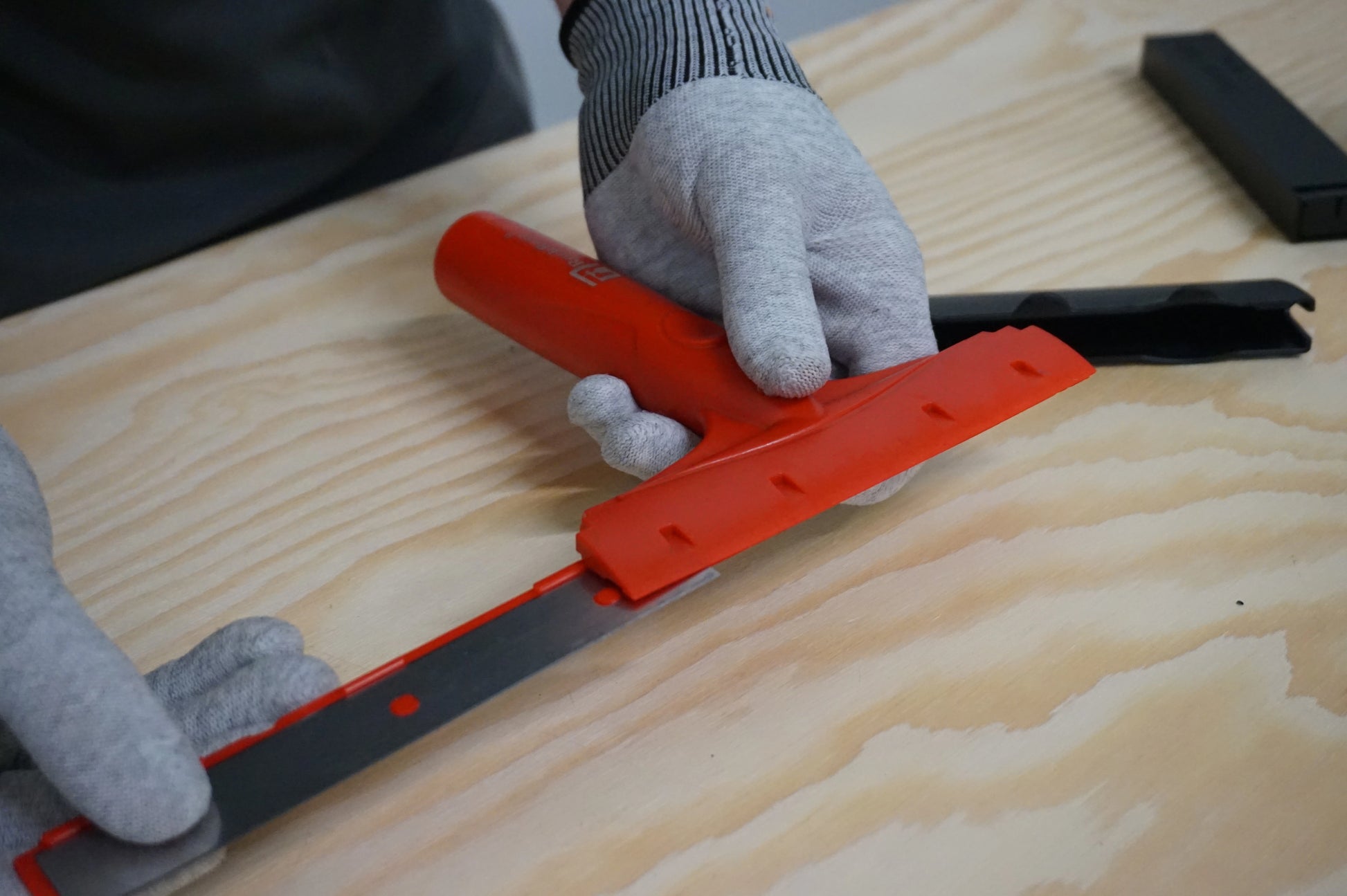 Person using a red squeegee with blades  on a wooden surface