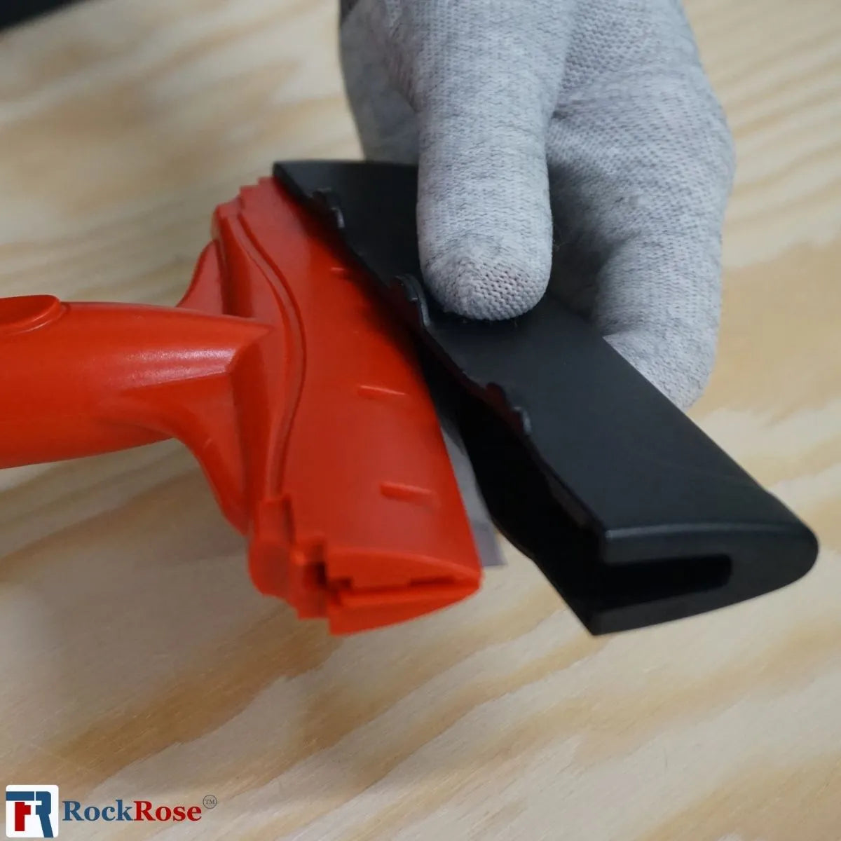 Red and black squeegee held by a gray glove on a wooden surface, with RockRose logo.