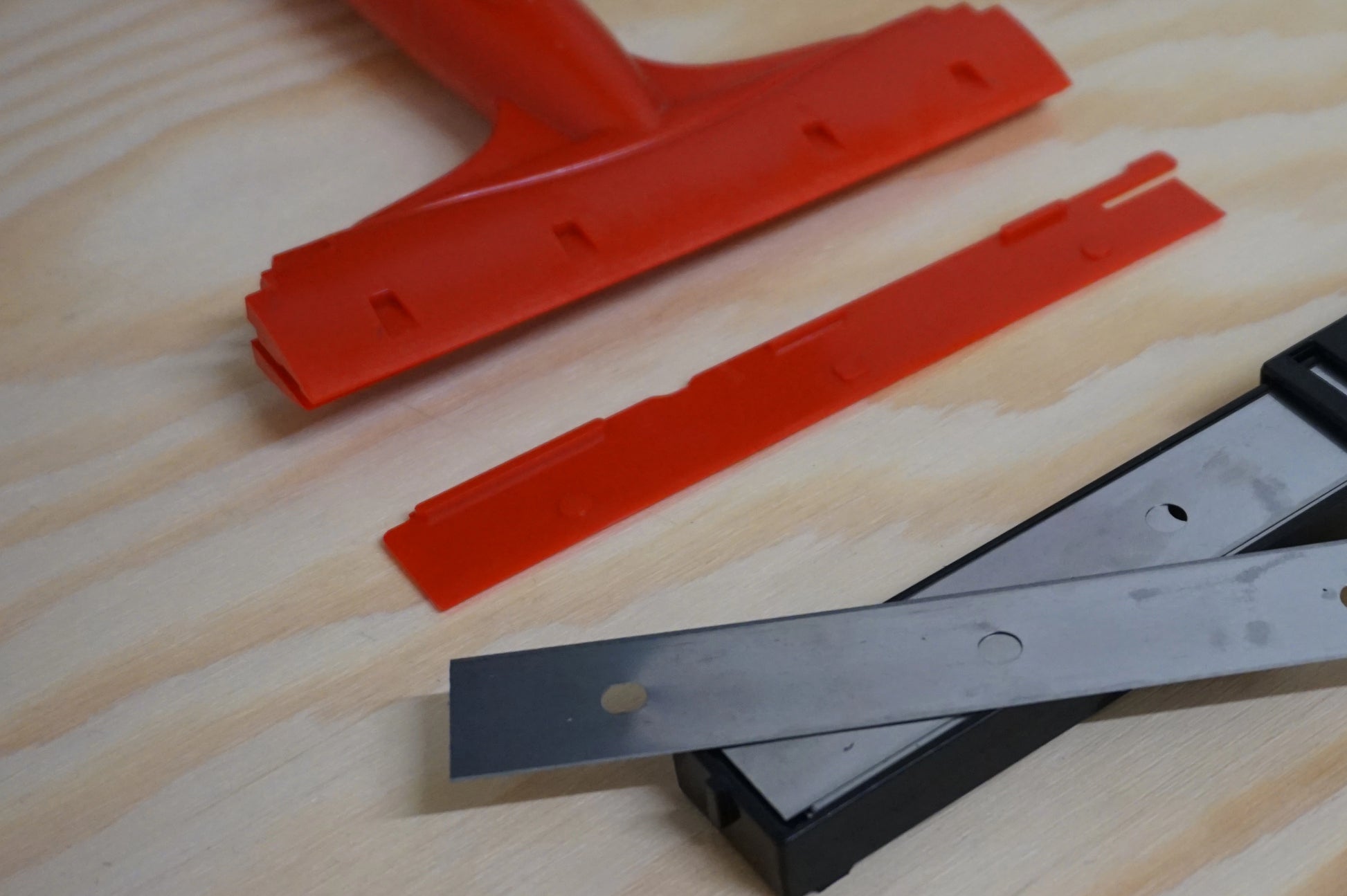 Red squeegee and metal blade on a wooden surface