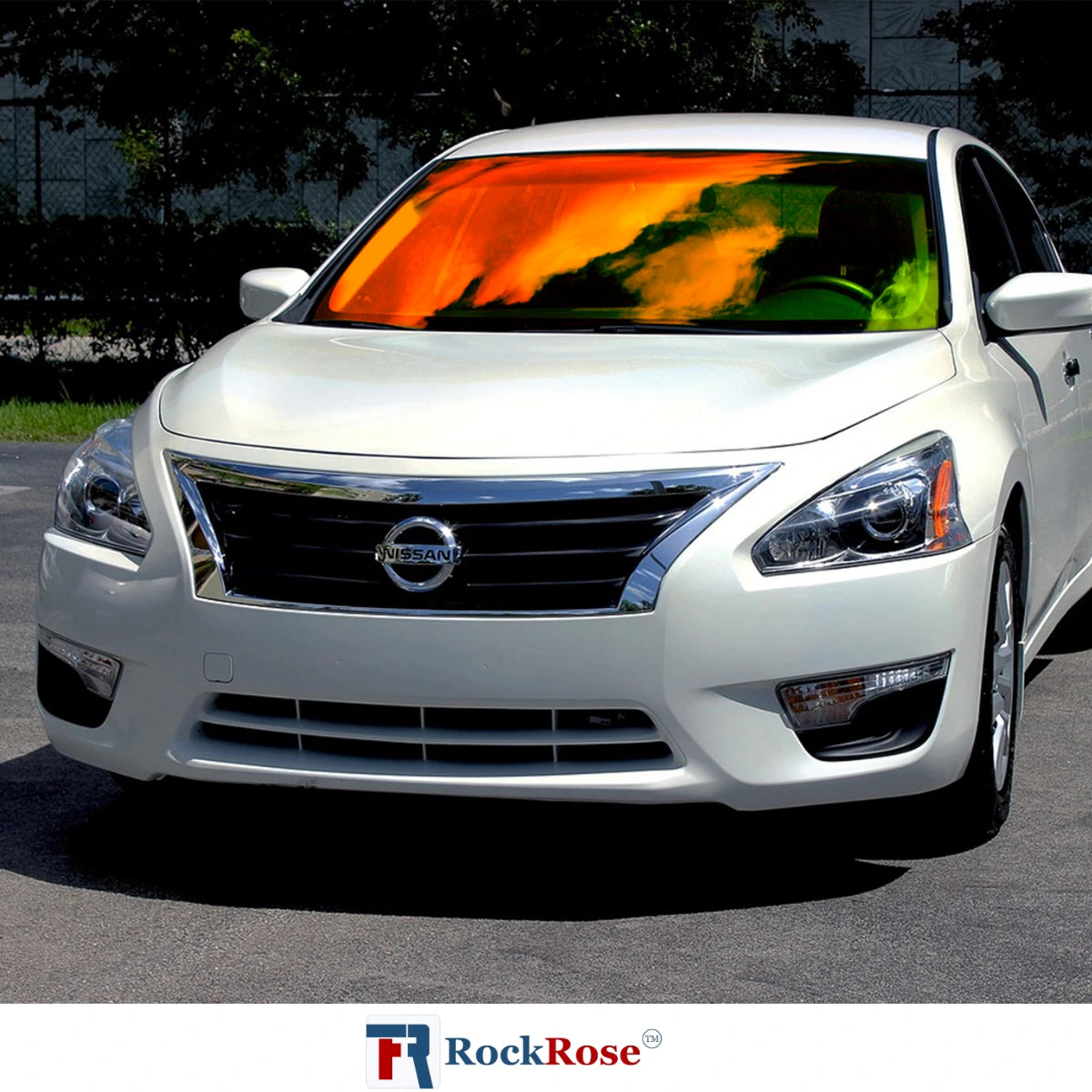 White Nissan car with a colorful sunshade on the windshield, parked outdoors.