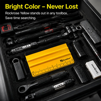 A black toolbox tray filled with various hand tools, including a bright yellow Rockrose yellow ruler in the center, surrounded by black sockets, wrenches, and other tools. Text at the top reads 'Bright Color - Never Lost' and 'Rockrose Yellow stands out in any toolbox.