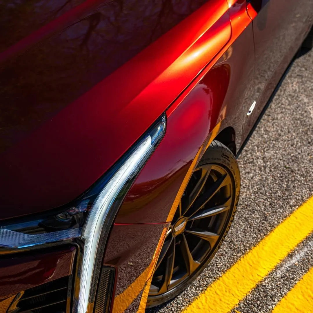 Close-up of a red car's front wheel and fender on a road with yellow lines.