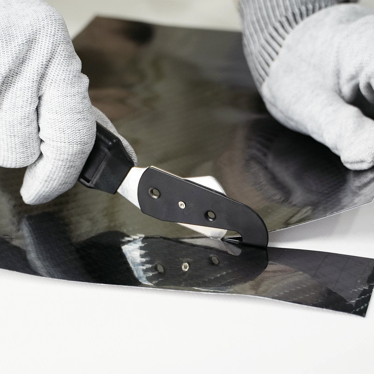 Person using a single vinyl cutter tool to black vinyl wrap on a surface