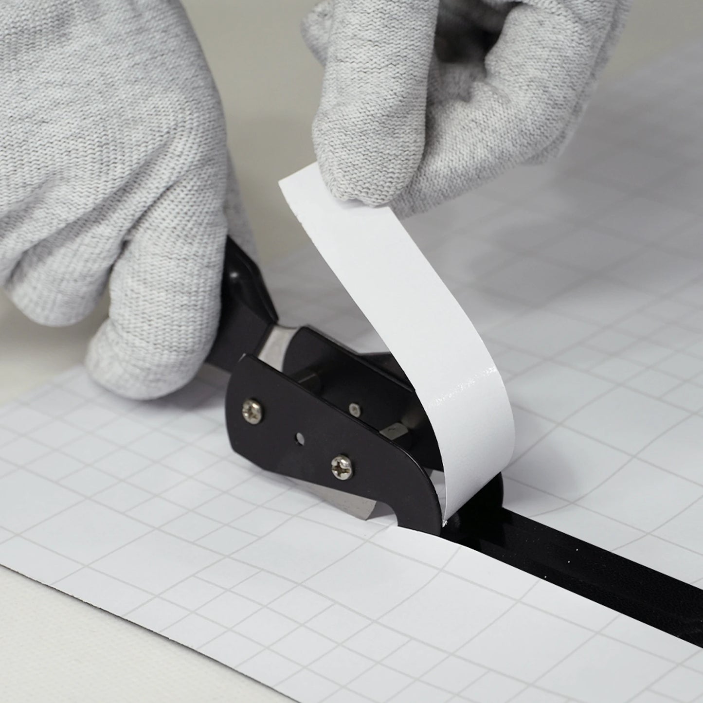 Person using a paper cutter slitter tool with gloves on a grid background