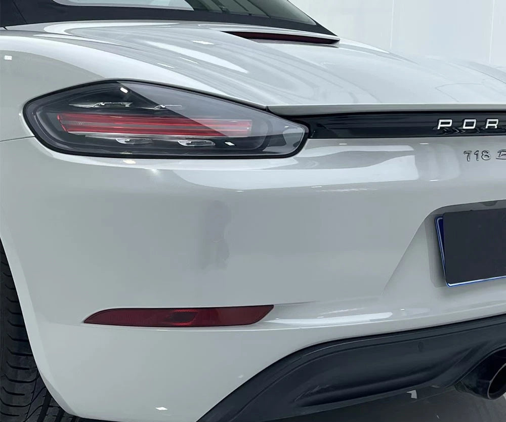 Close-up of a white car's headlight and badge with 'Porsche' branding.