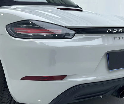 Close-up of a white car's headlight and badge with 'Porsche' branding.