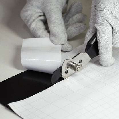 Person cutting black wrap with a cutter tool on a white surface